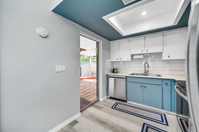 kitchen featuring a sink, a tray ceiling, stainless steel dishwasher, backsplash, and light countertops