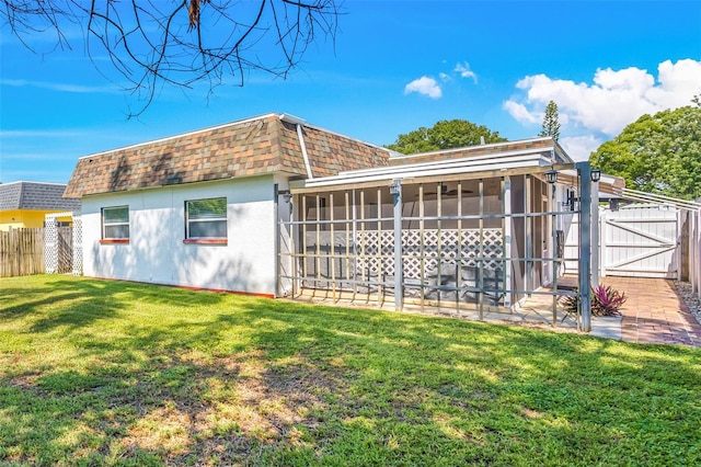 back of property with a shingled roof, fence, a lawn, mansard roof, and a sunroom