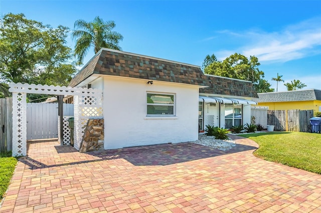 back of property featuring stucco siding, a lawn, mansard roof, fence, and a shingled roof