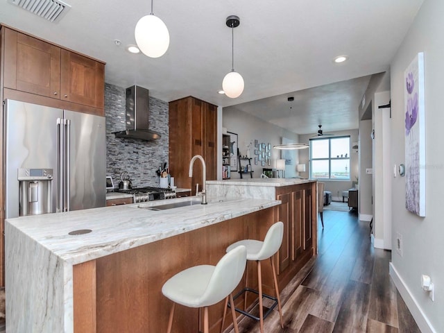 kitchen with visible vents, backsplash, wall chimney range hood, high end refrigerator, and a sink