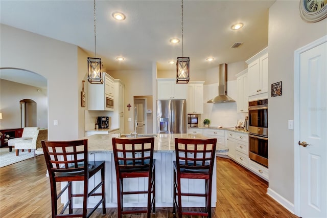 kitchen featuring visible vents, arched walkways, dark wood-type flooring, appliances with stainless steel finishes, and wall chimney exhaust hood