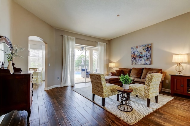 living area with dark wood-style floors, arched walkways, and a healthy amount of sunlight