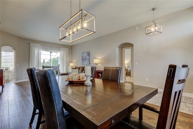 dining room with a notable chandelier, wood finished floors, arched walkways, and baseboards