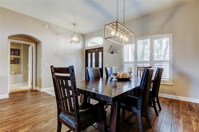 dining space with wood finished floors, arched walkways, a wealth of natural light, and baseboards