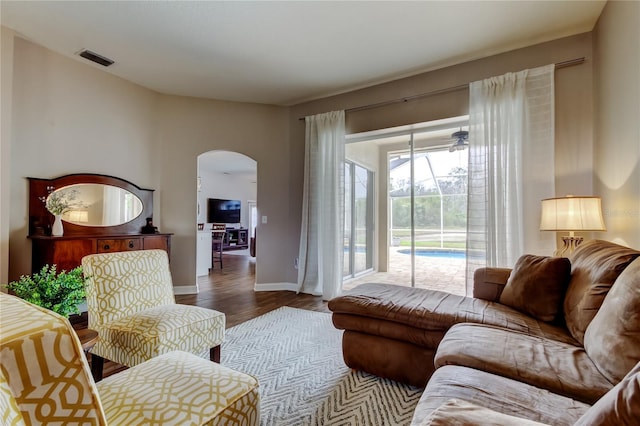 living room with arched walkways, visible vents, dark wood finished floors, and baseboards