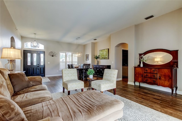 living area with arched walkways, visible vents, a notable chandelier, and wood finished floors