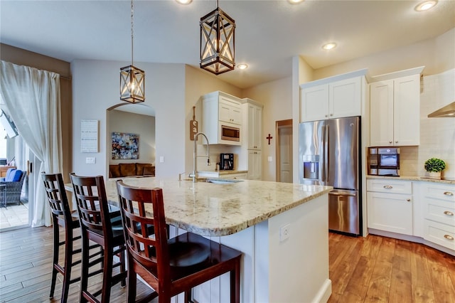 kitchen featuring a sink, white cabinetry, light wood-style floors, appliances with stainless steel finishes, and light stone countertops