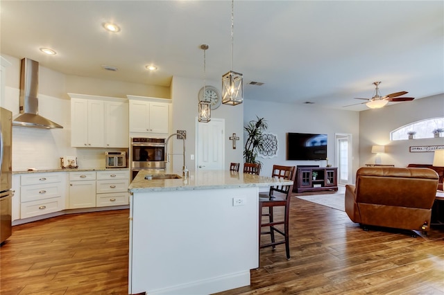 kitchen featuring visible vents, light stone counters, wood finished floors, a breakfast bar area, and wall chimney exhaust hood