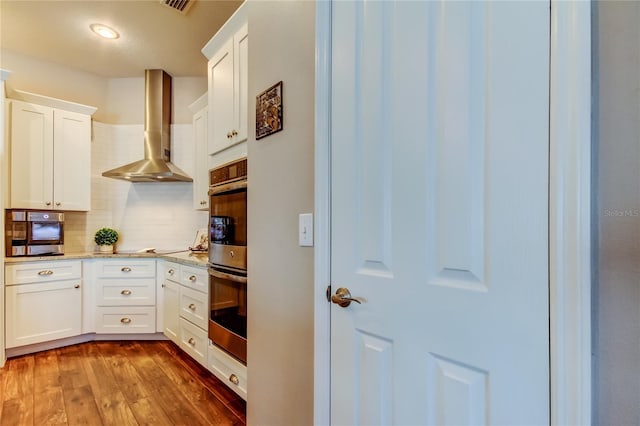 kitchen featuring dark wood finished floors, light stone counters, decorative backsplash, white cabinets, and wall chimney exhaust hood