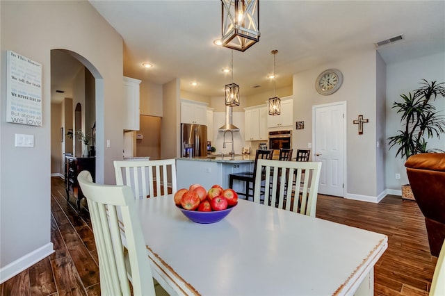 dining space with arched walkways, visible vents, baseboards, and dark wood-style flooring