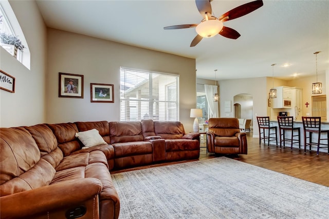 living area featuring arched walkways, plenty of natural light, a ceiling fan, and wood finished floors