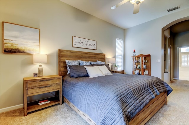 carpeted bedroom with visible vents, arched walkways, baseboards, and a ceiling fan