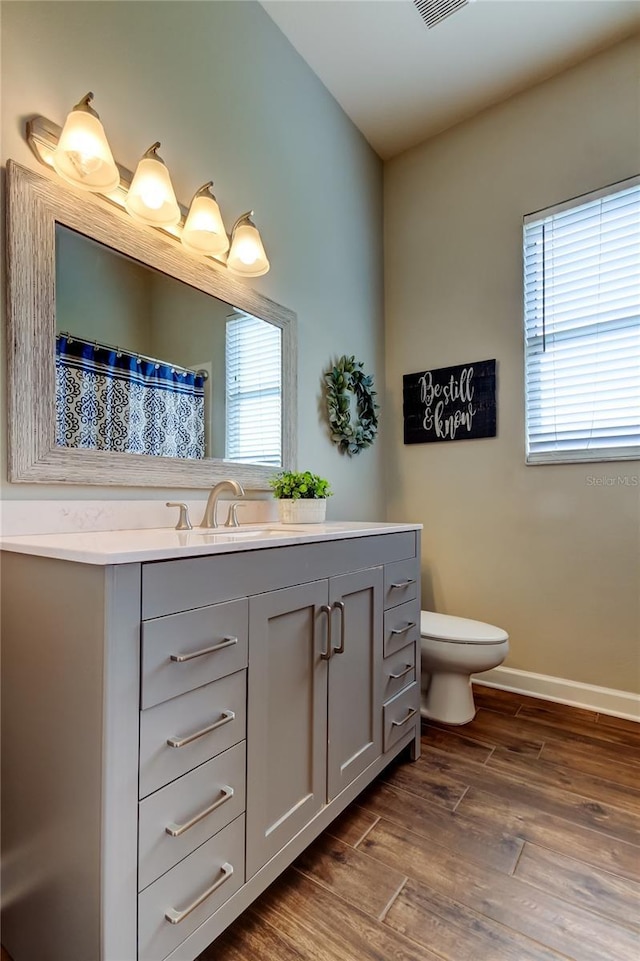 bathroom with vanity, wood finished floors, baseboards, lofted ceiling, and toilet