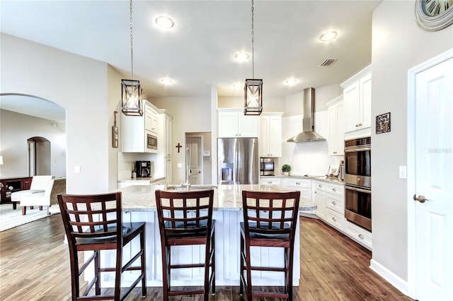 kitchen with visible vents, a breakfast bar, arched walkways, stainless steel appliances, and wall chimney exhaust hood