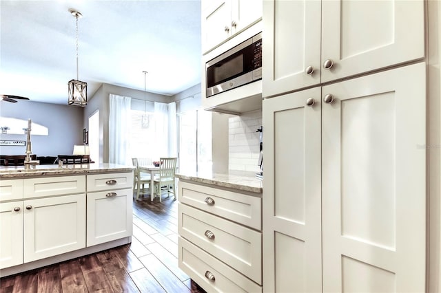 kitchen featuring stainless steel microwave, dark wood-style floors, white cabinetry, decorative backsplash, and hanging light fixtures