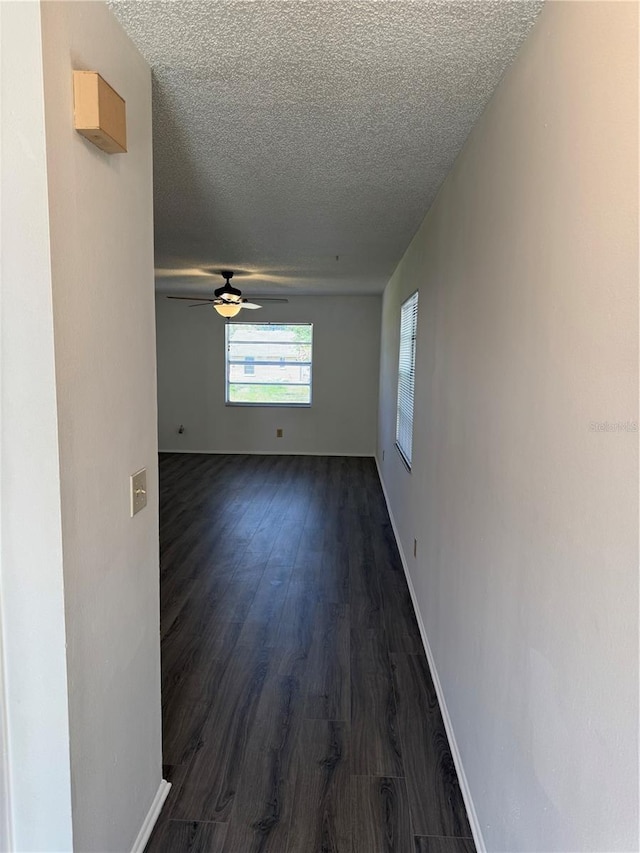 spare room with ceiling fan, a textured ceiling, dark wood-type flooring, and baseboards