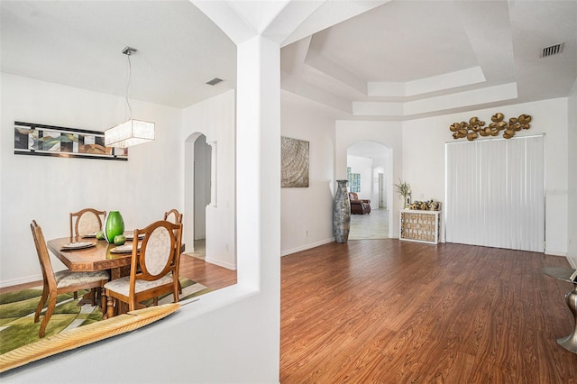 dining space featuring visible vents, baseboards, wood finished floors, arched walkways, and a raised ceiling