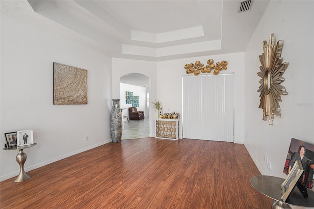 empty room with visible vents, baseboards, wood finished floors, arched walkways, and a raised ceiling