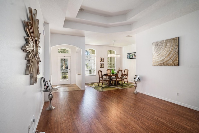 foyer with visible vents, baseboards, a tray ceiling, arched walkways, and wood-type flooring