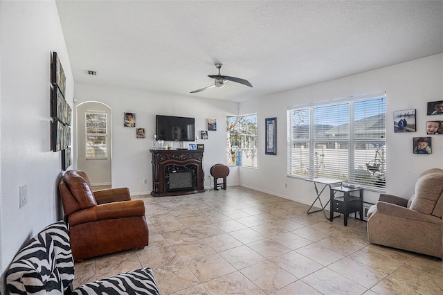 living area featuring a glass covered fireplace, plenty of natural light, and ceiling fan