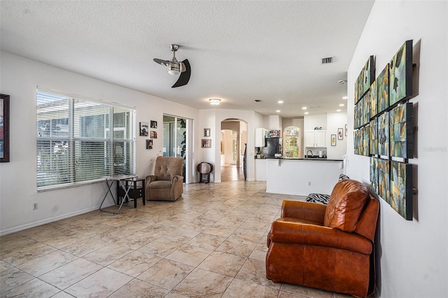 living area with arched walkways, visible vents, a textured ceiling, and a ceiling fan