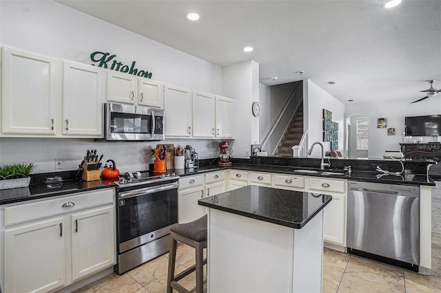 kitchen featuring a sink, a kitchen island, white cabinetry, appliances with stainless steel finishes, and a peninsula