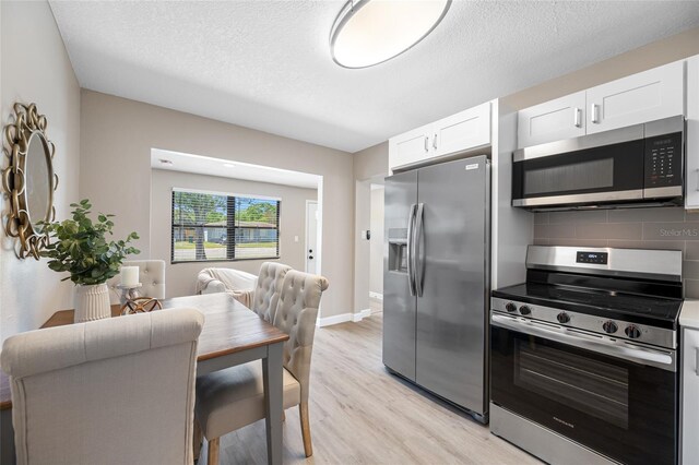 217 Emerald Ln, Largo, FL 33771 - kitchen with light wood-type flooring, decorative backsplash, white cabinetry, and stainless steel appliances