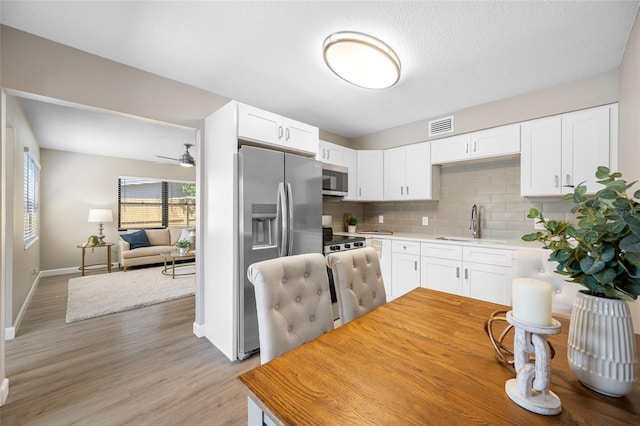 217 Emerald Ln, Largo, FL 33771 - kitchen with tasteful backsplash, stainless steel appliances, visible vents, white cabinets, and light wood-style floors