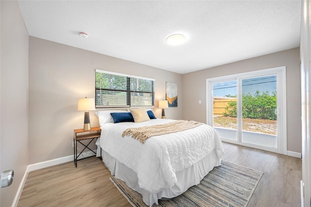 217 Emerald Ln, Largo, FL 33771 - bedroom featuring baseboards, a textured ceiling, access to exterior, and light wood-style flooring