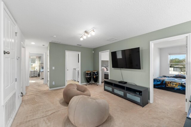 living area featuring baseboards, washing machine and dryer, a textured ceiling, and light colored carpet