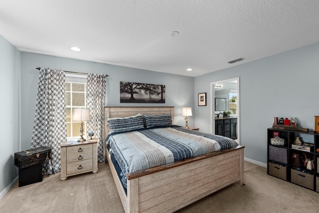bedroom with visible vents, baseboards, ensuite bathroom, light colored carpet, and a textured ceiling