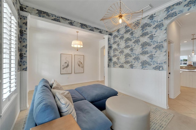 living room with light tile patterned floors, wallpapered walls, arched walkways, ornamental molding, and wainscoting