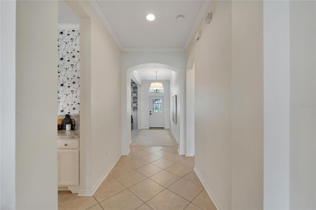 hallway featuring light tile patterned floors, baseboards, arched walkways, and ornamental molding