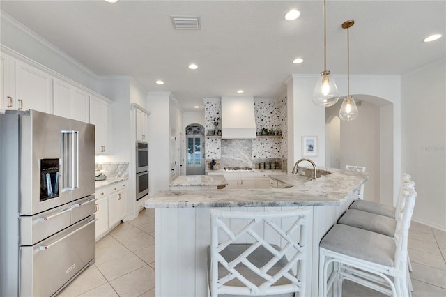 kitchen with premium range hood, visible vents, stainless steel appliances, arched walkways, and light tile patterned floors