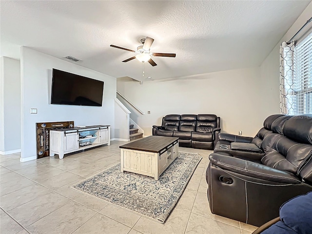 living room featuring visible vents, baseboards, stairs, a textured ceiling, and a ceiling fan