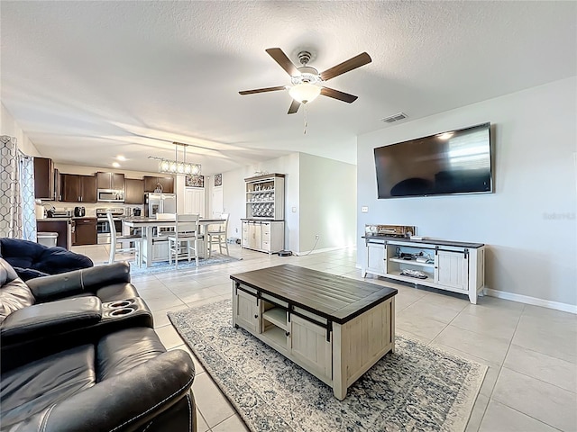 living room with visible vents, baseboards, light tile patterned floors, ceiling fan with notable chandelier, and a textured ceiling