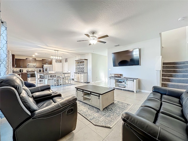 living area featuring stairway, visible vents, light tile patterned flooring, a textured ceiling, and ceiling fan with notable chandelier