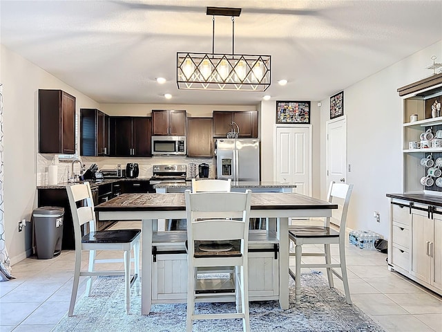 kitchen featuring baseboards, light tile patterned flooring, dark brown cabinets, appliances with stainless steel finishes, and backsplash