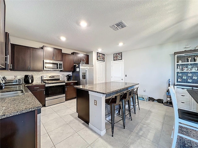 kitchen with visible vents, a sink, stainless steel appliances, dark brown cabinets, and a kitchen breakfast bar