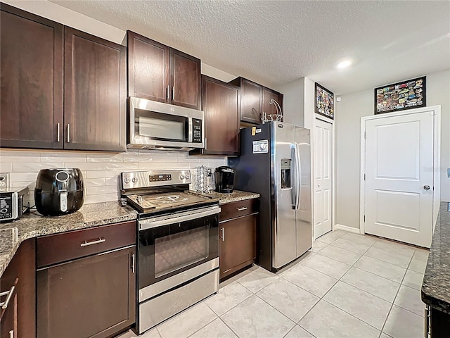 kitchen with tasteful backsplash, dark brown cabinets, stainless steel appliances, and light stone counters