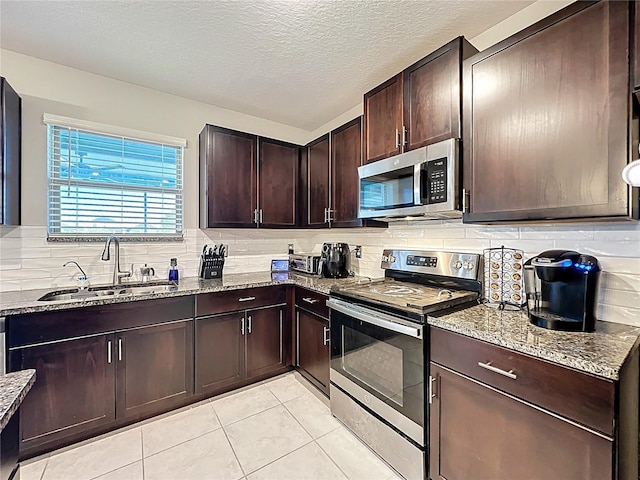 kitchen with a sink, tasteful backsplash, stainless steel appliances, dark brown cabinetry, and light stone countertops