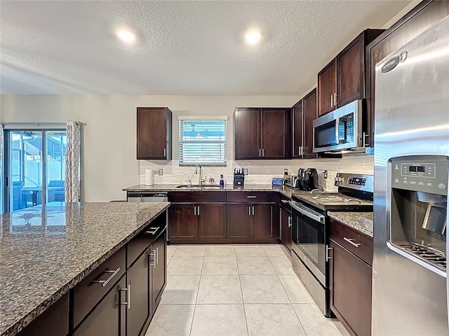 kitchen with dark stone countertops, light tile patterned flooring, a sink, decorative backsplash, and stainless steel appliances