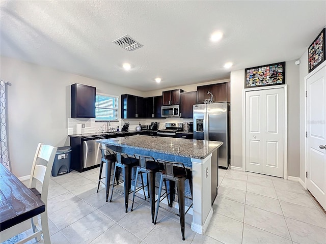 kitchen featuring light tile patterned floors, visible vents, a kitchen island, appliances with stainless steel finishes, and a kitchen breakfast bar