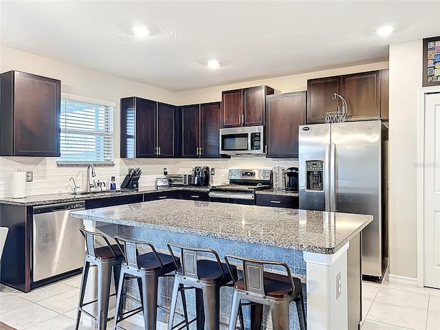 kitchen with stone countertops, appliances with stainless steel finishes, a breakfast bar area, and a sink