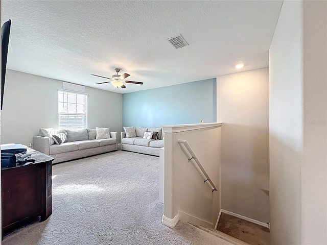 living room featuring a textured ceiling, carpet flooring, visible vents, and ceiling fan