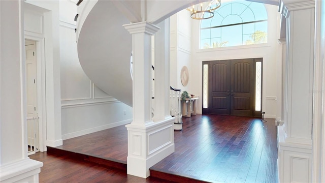 entrance foyer with dark wood-type flooring, arched walkways, an inviting chandelier, a decorative wall, and decorative columns