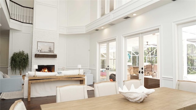 dining area with wood finished floors, a towering ceiling, a fireplace, and a decorative wall