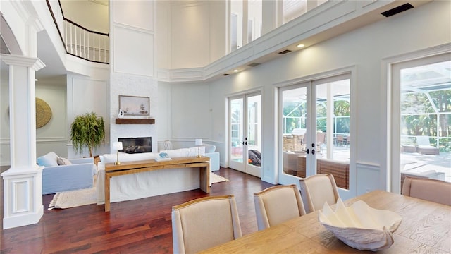 dining space with dark wood finished floors, french doors, a large fireplace, a decorative wall, and decorative columns