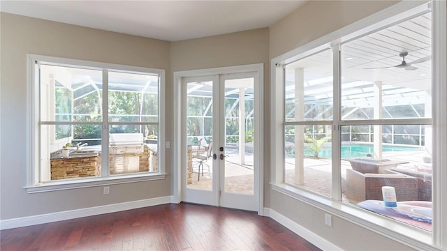 doorway to outside with dark wood-style floors, a ceiling fan, and baseboards