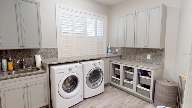 laundry room with cabinet space, washer and dryer, light wood-style flooring, and a sink